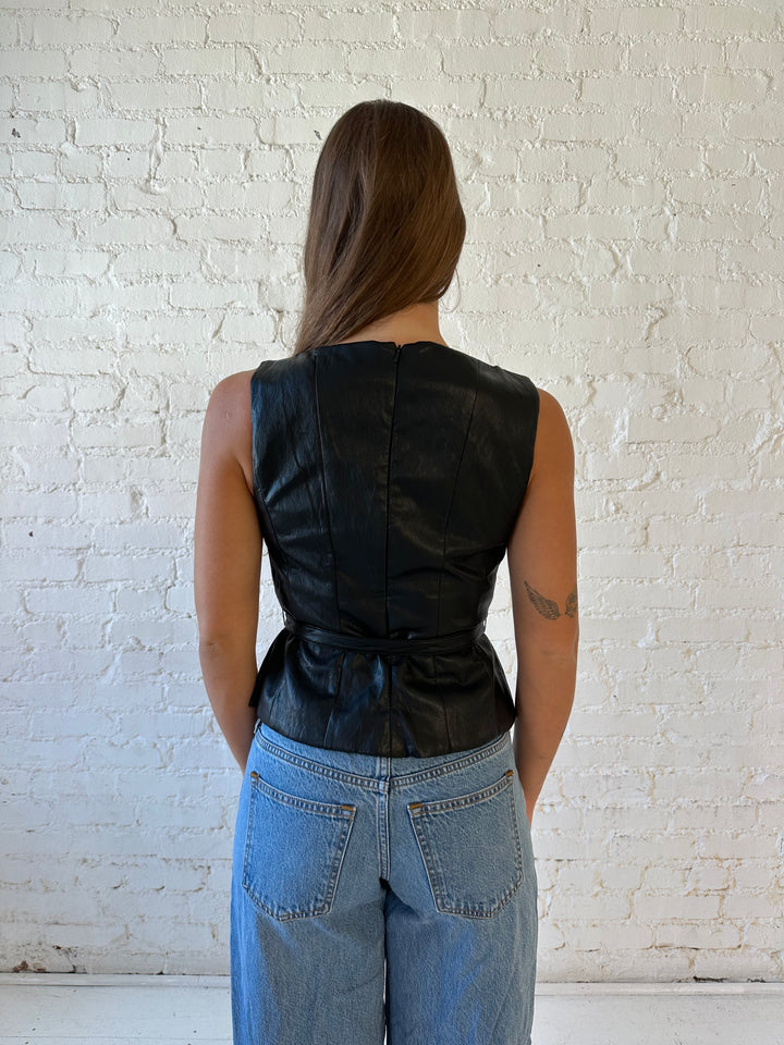 Woman wearing black leather top with belted waist detail.