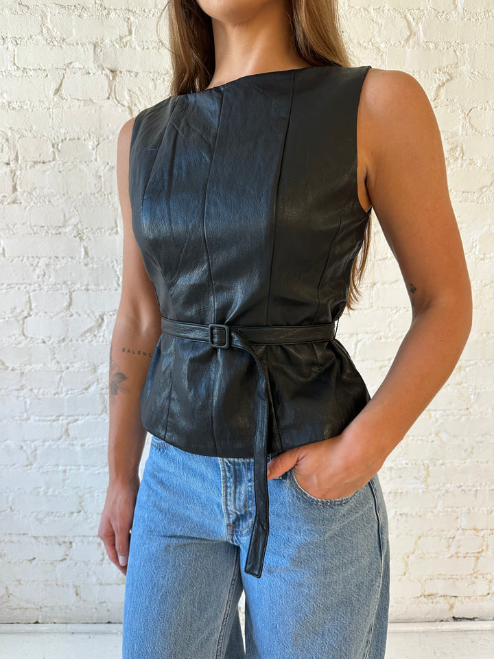 Woman wearing black leather top with belted waist detail.