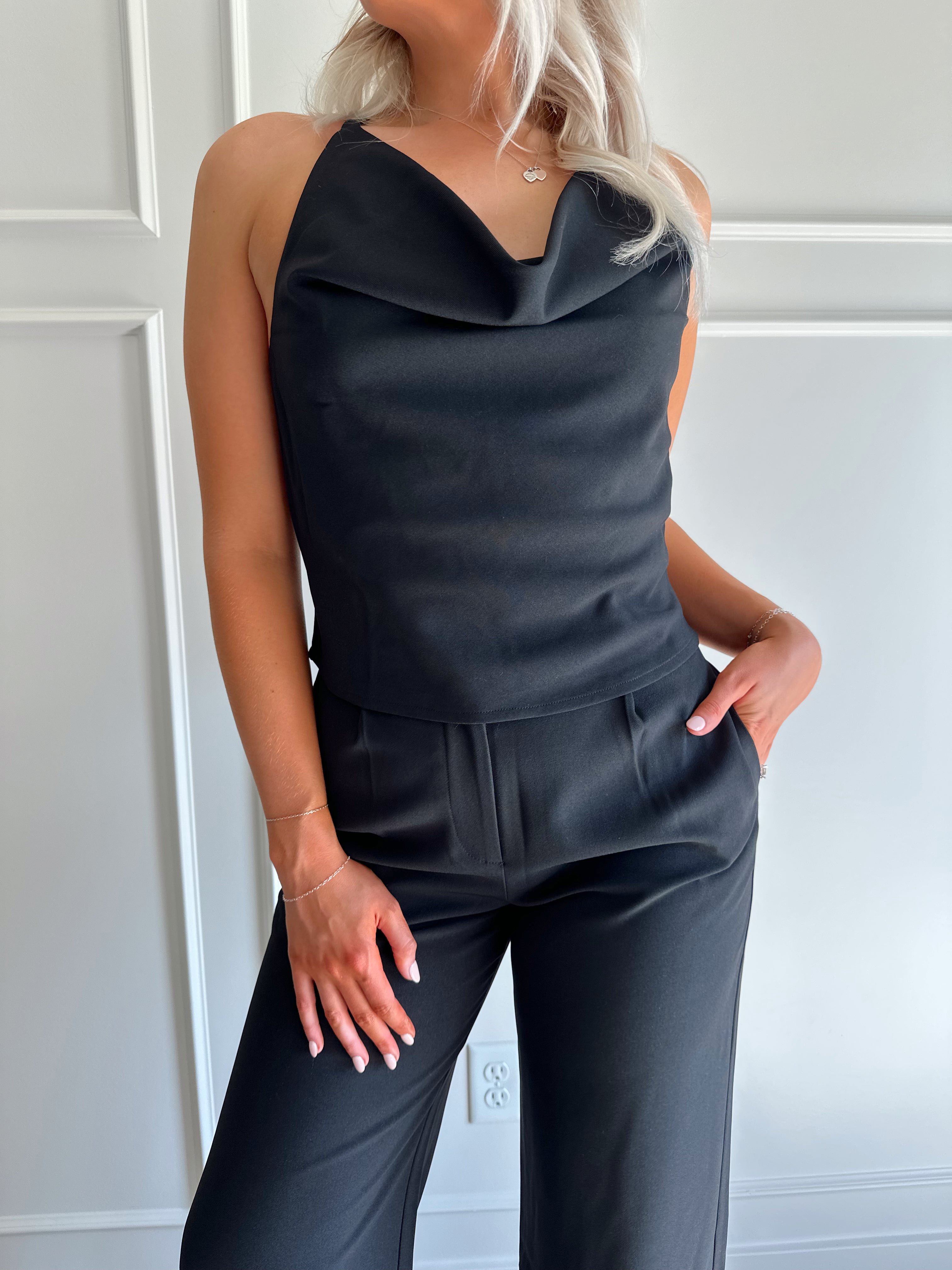 Woman wearing black two piece set with cowl neck top, and tailored wide leg pant.