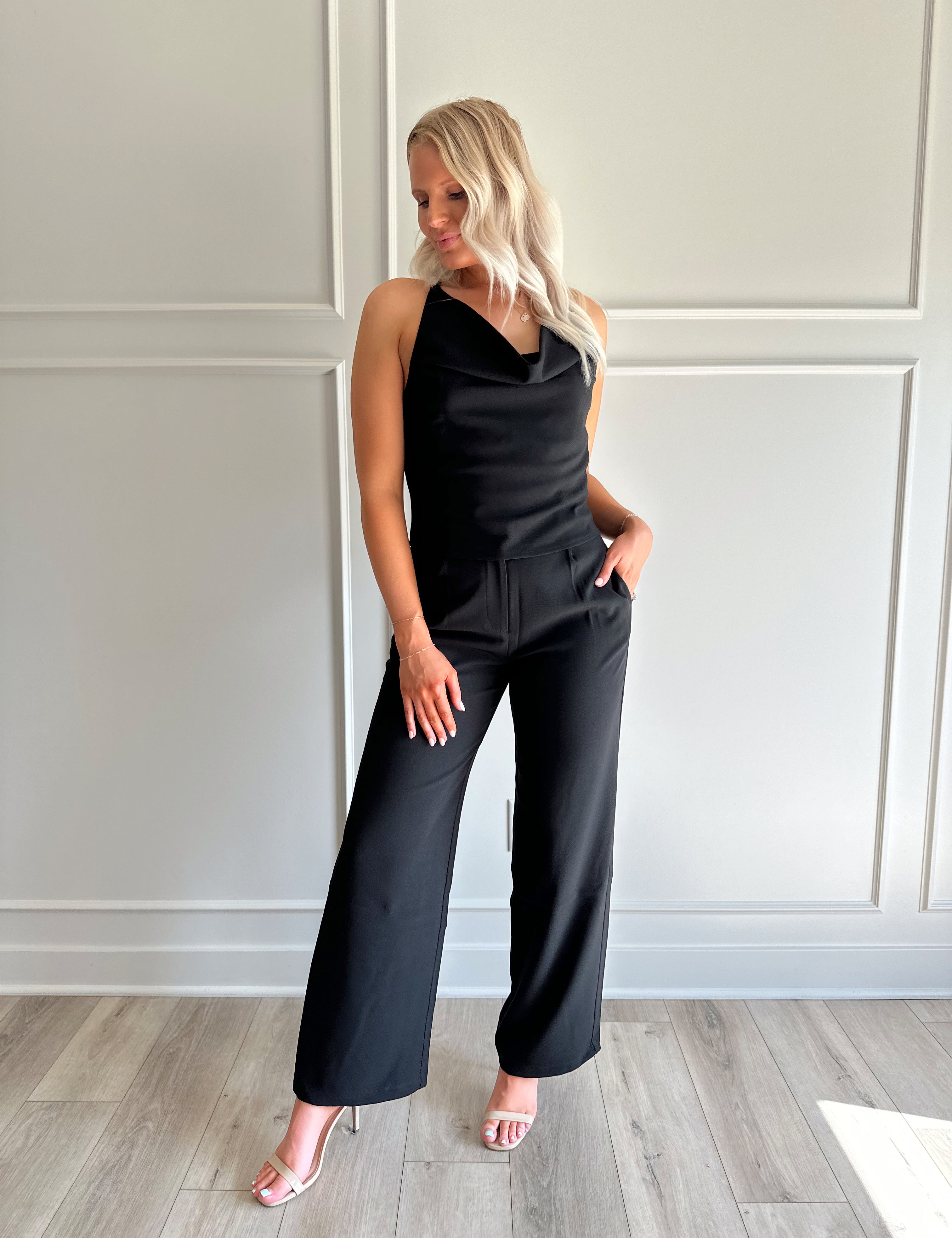 Woman wearing black two piece set with cowl neck top, and tailored wide leg pant.