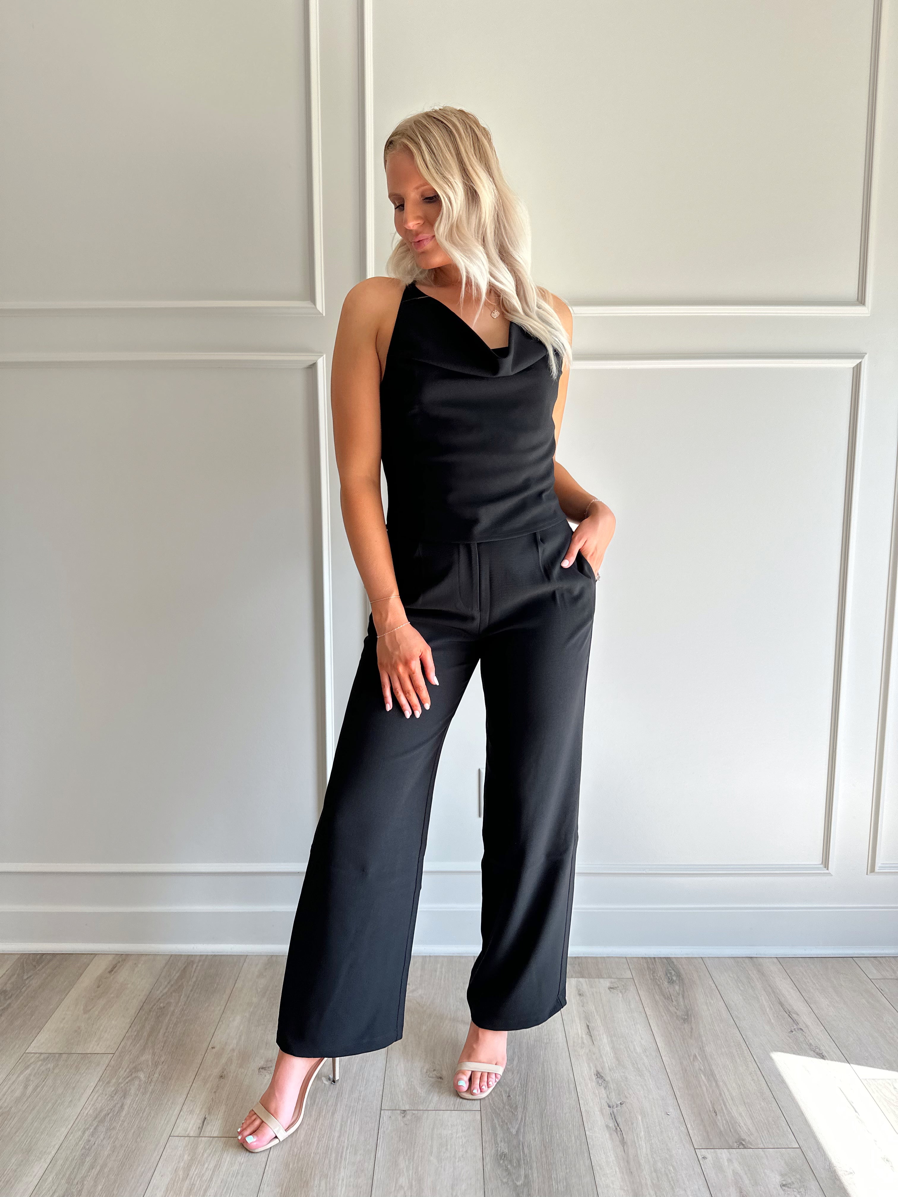Woman wearing black two piece set with cowl neck top, and tailored wide leg pant.