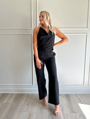 Woman wearing black two piece set with cowl neck top, and tailored wide leg pant.