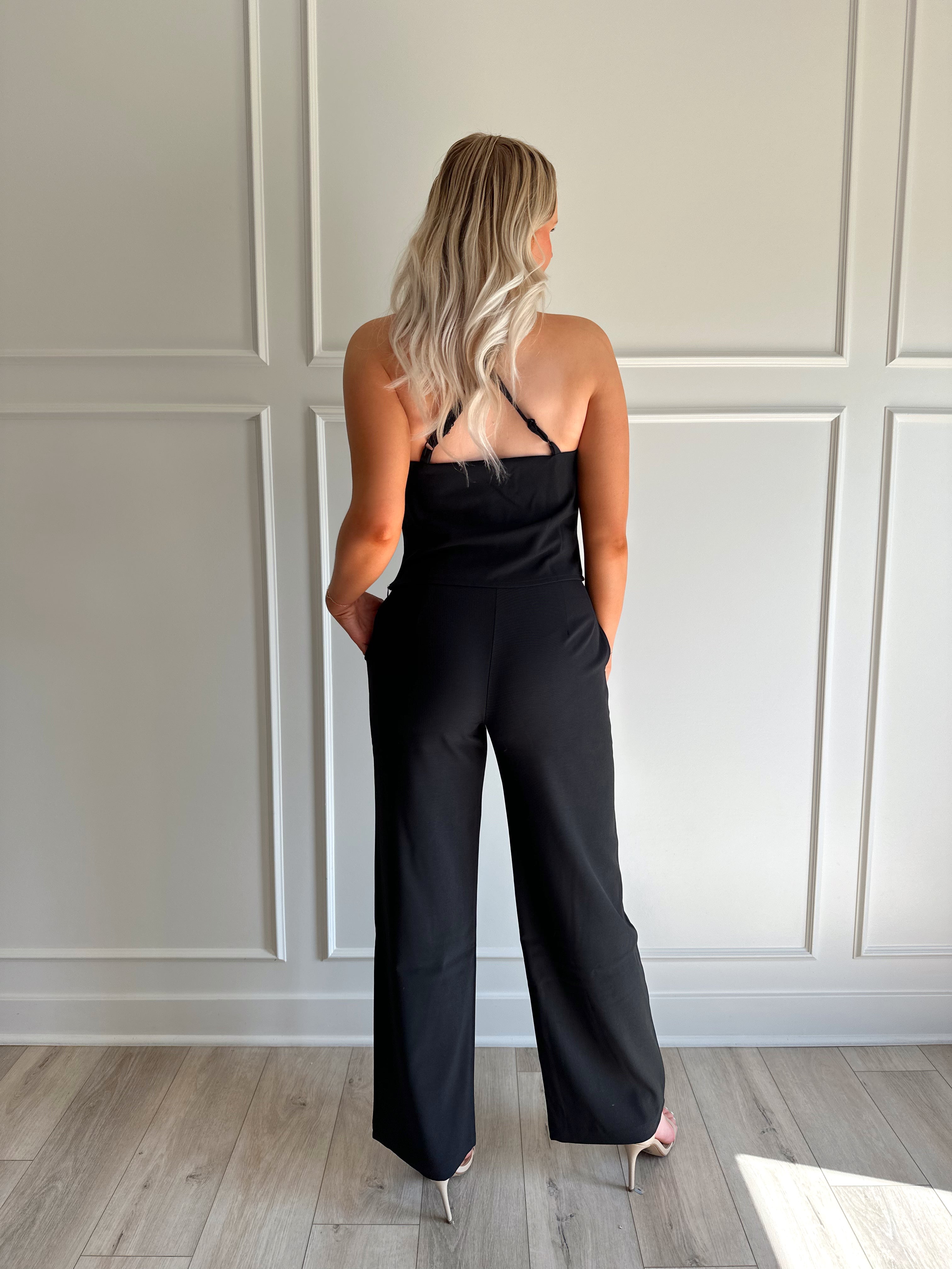 Woman wearing black two piece set with cowl neck top, and tailored wide leg pant.