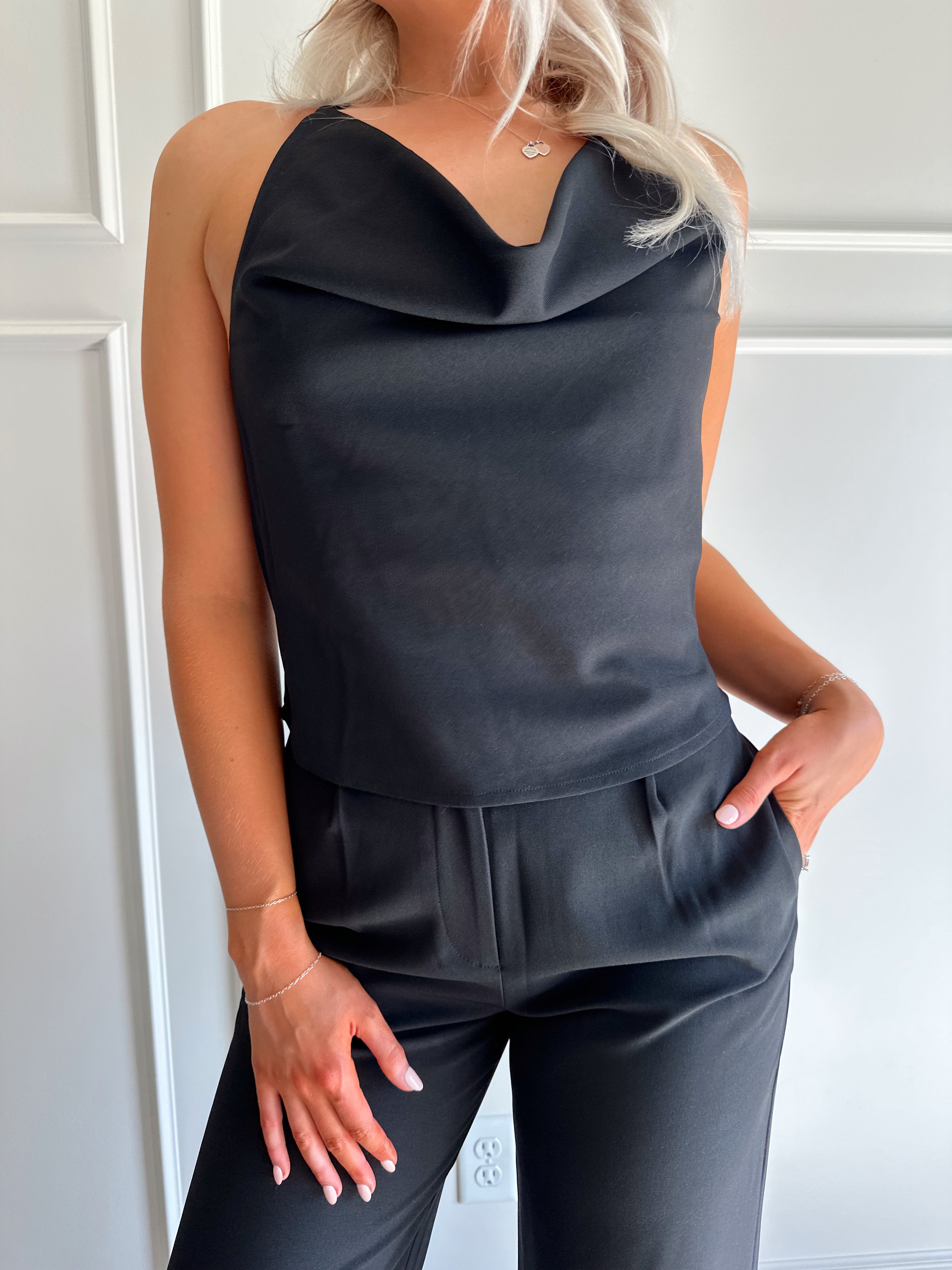 Woman wearing black two piece set with cowl neck top, and tailored wide leg pant.