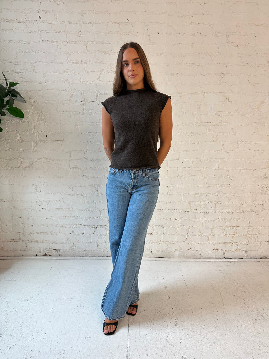 Woman wearing brown knit cap sleeve top with medium wash jeans.