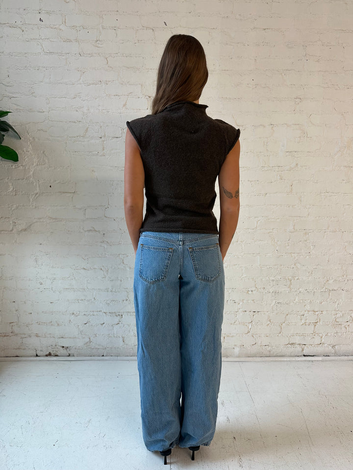 Woman wearing brown knit cap sleeve top with medium wash jeans.