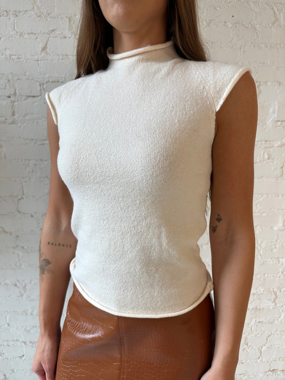 Woman wearing cream knit cap sleeve top and cognac leather mini skirt. 