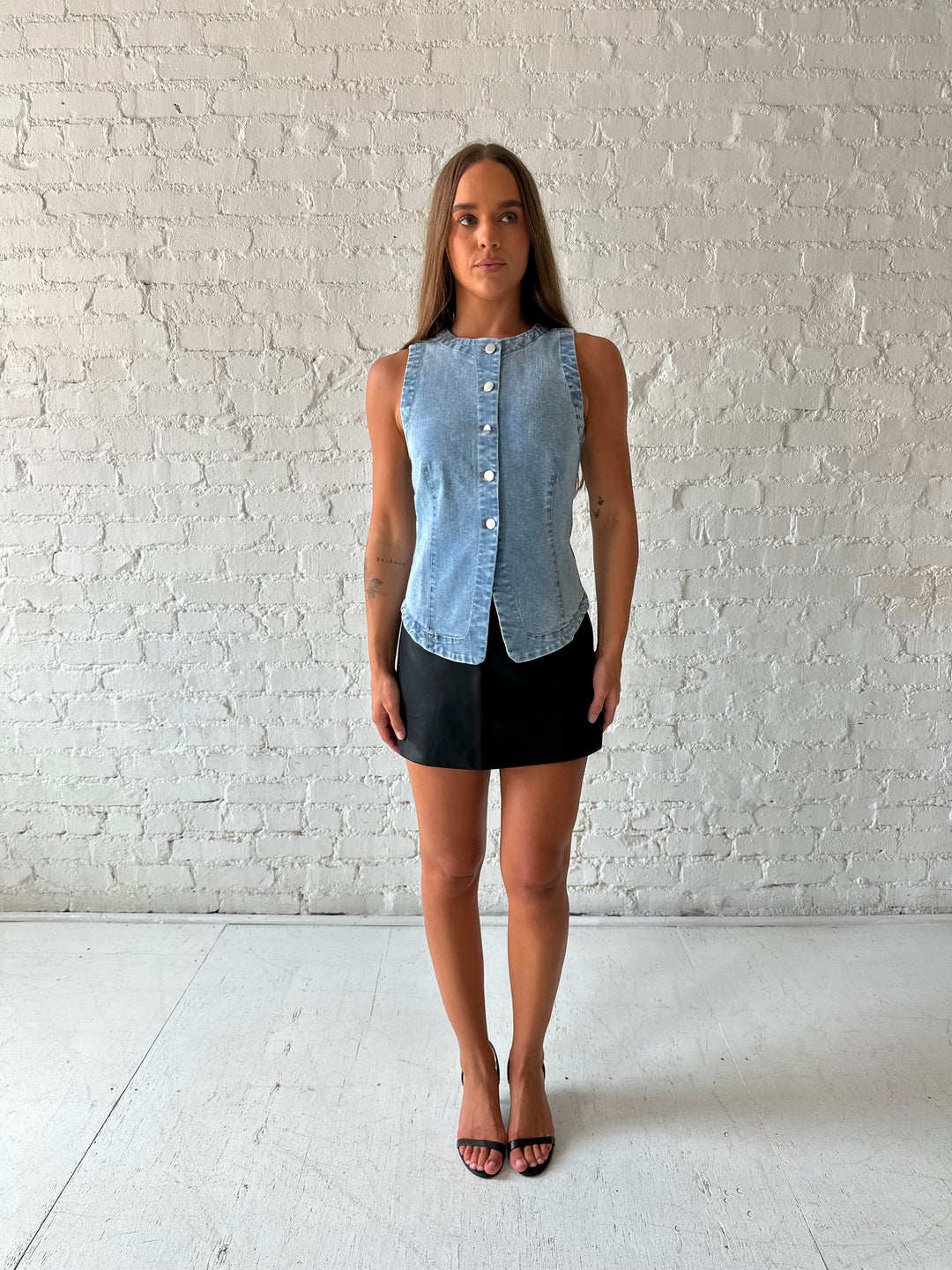 Woman wearing denim button down top with black leather mini skort. 