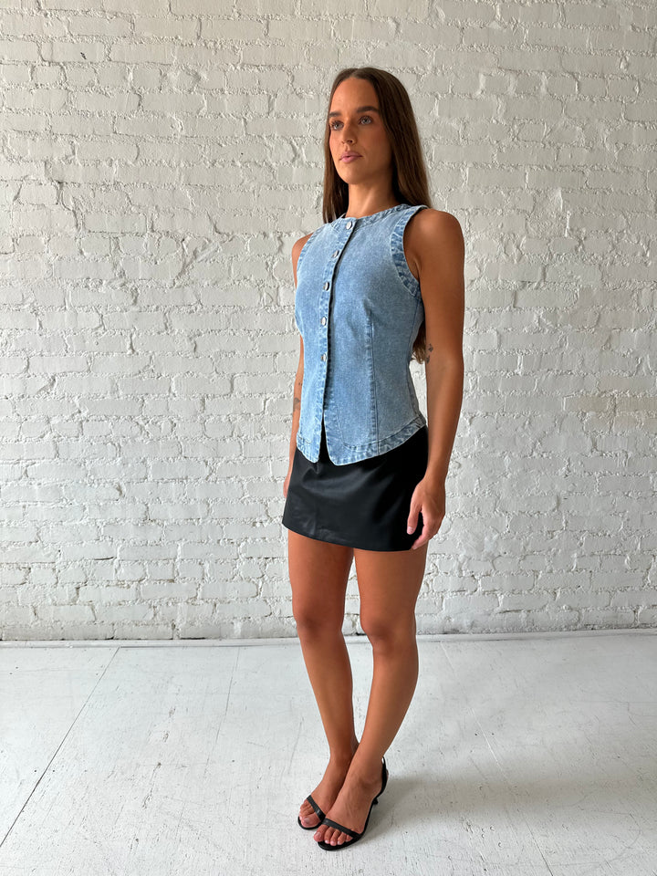 Woman wearing denim button down top with black leather mini skort. 