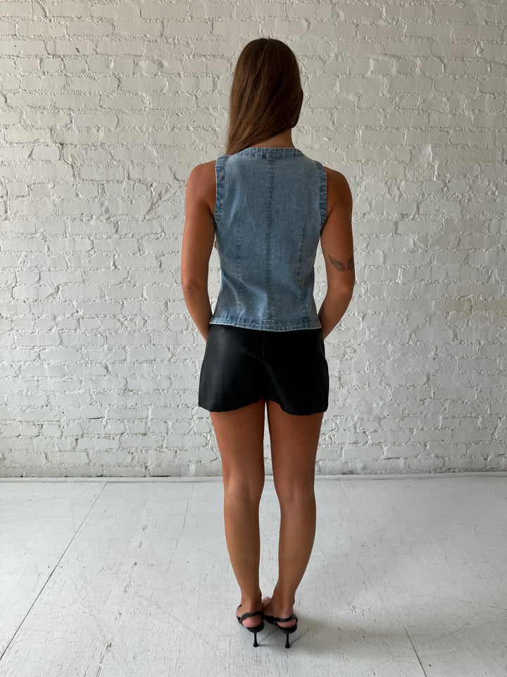 Woman wearing denim button down top with black leather mini skort. 