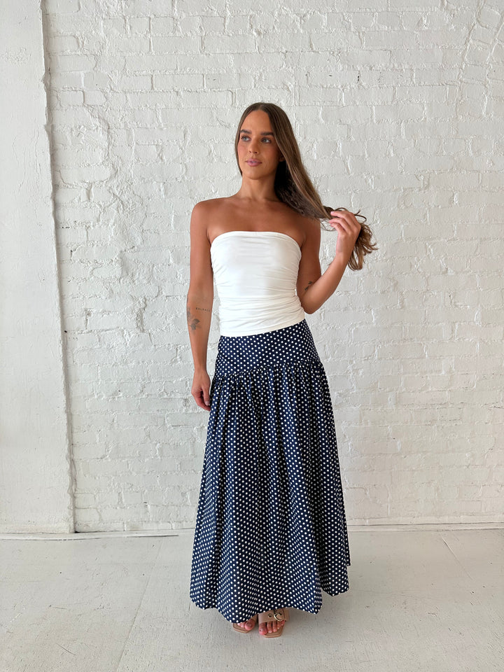 Woman wearing navy polka dot maxi skirt with white ruched tube top.