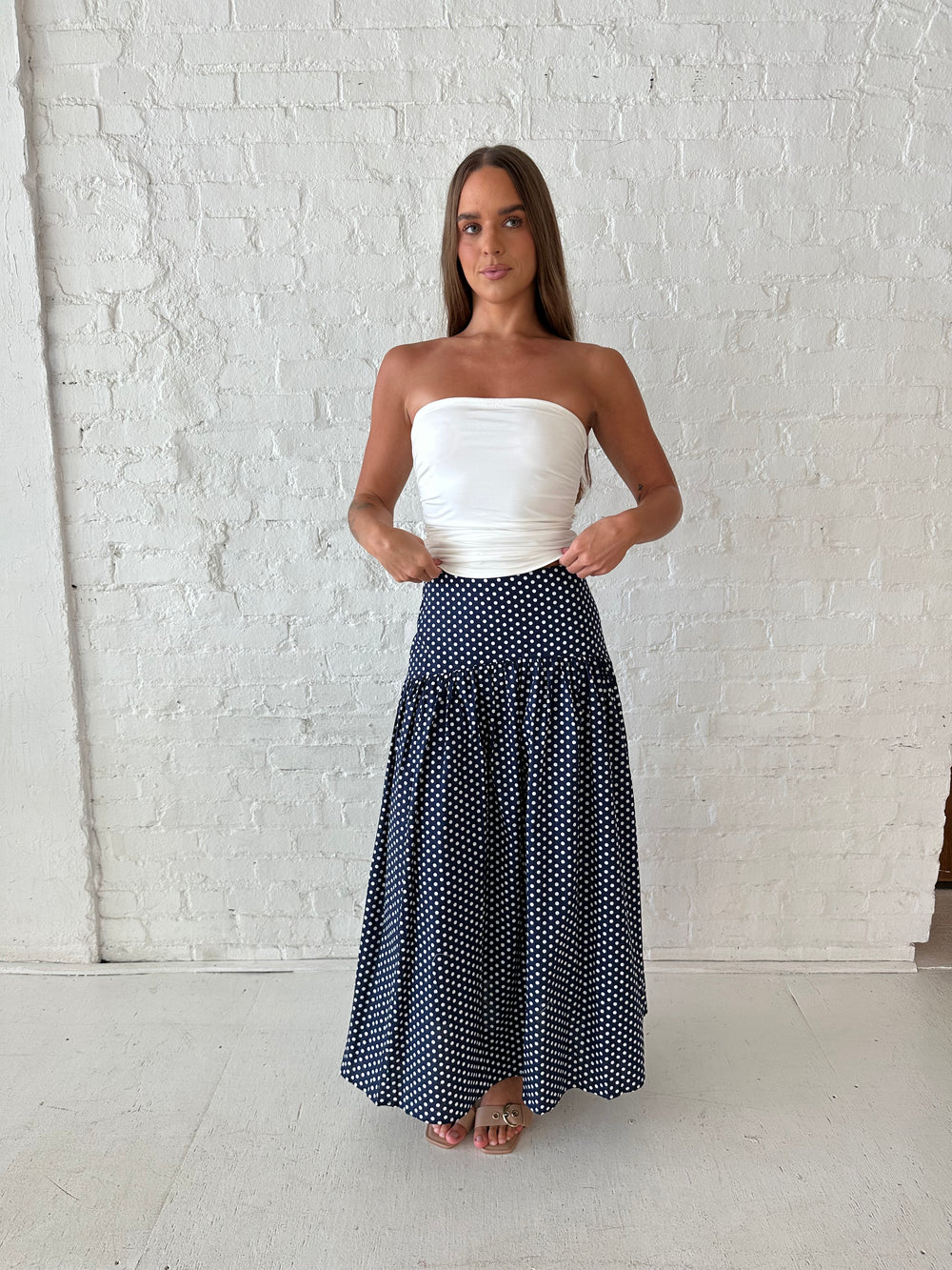 Woman wearing navy polka dot maxi skirt with white ruched tube top.