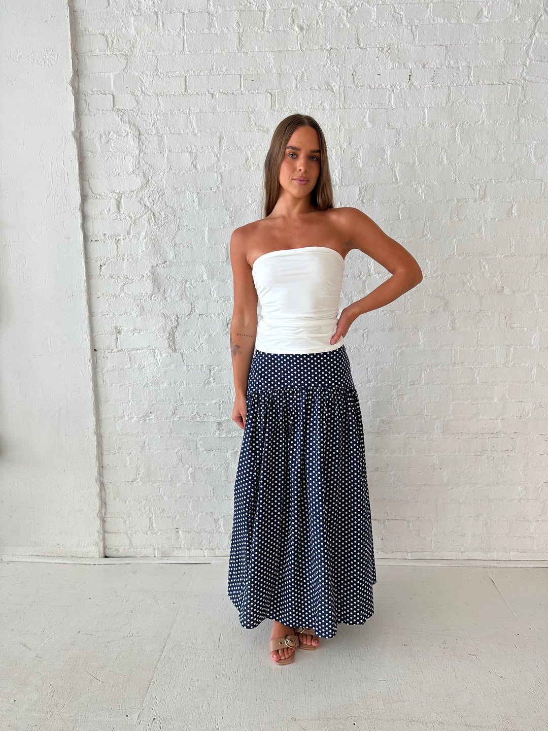Woman wearing navy polka dot maxi skirt with white ruched tube top.