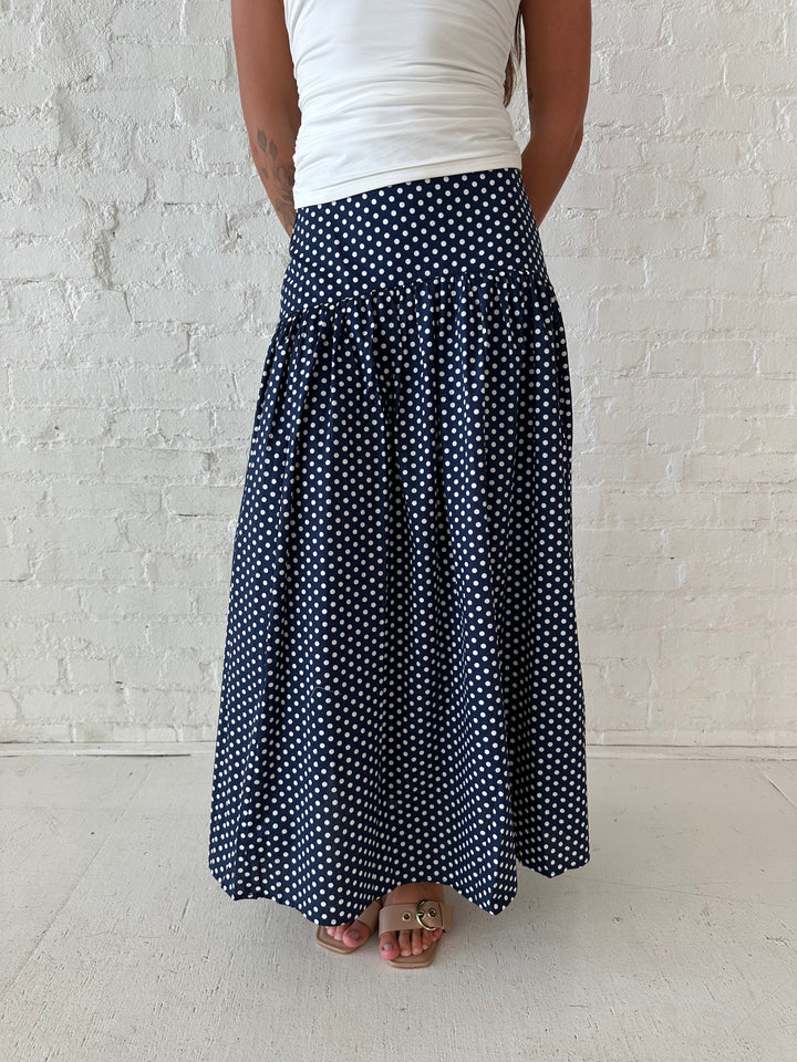 Woman wearing navy polka dot maxi skirt with white ruched tube top.