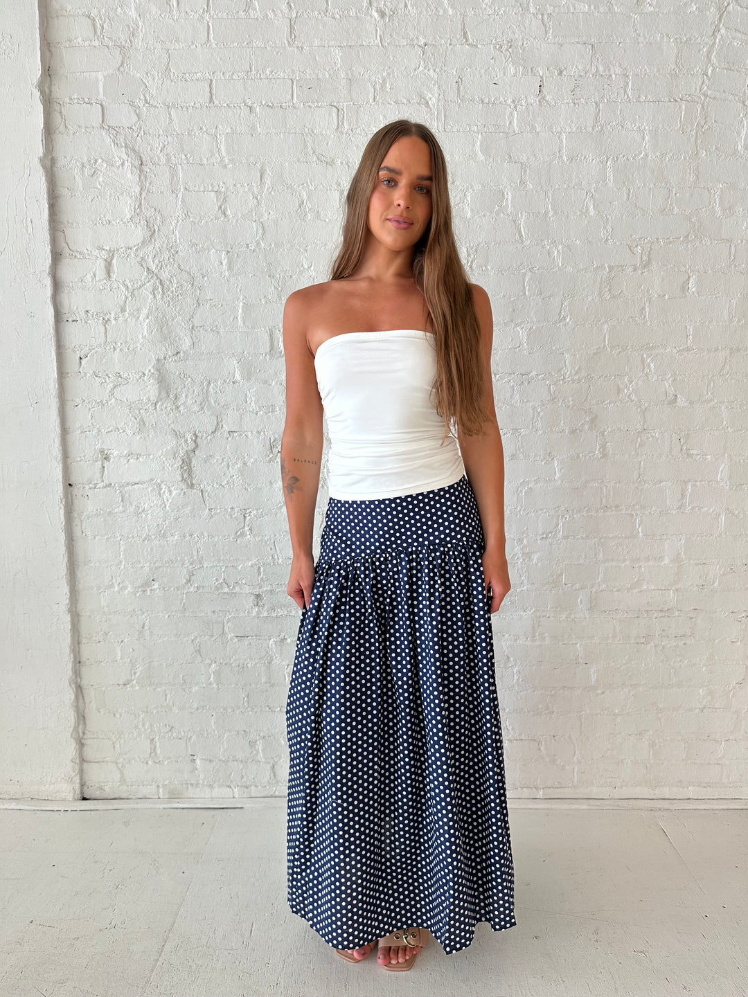 Woman wearing navy polka dot maxi skirt with white ruched tube top.