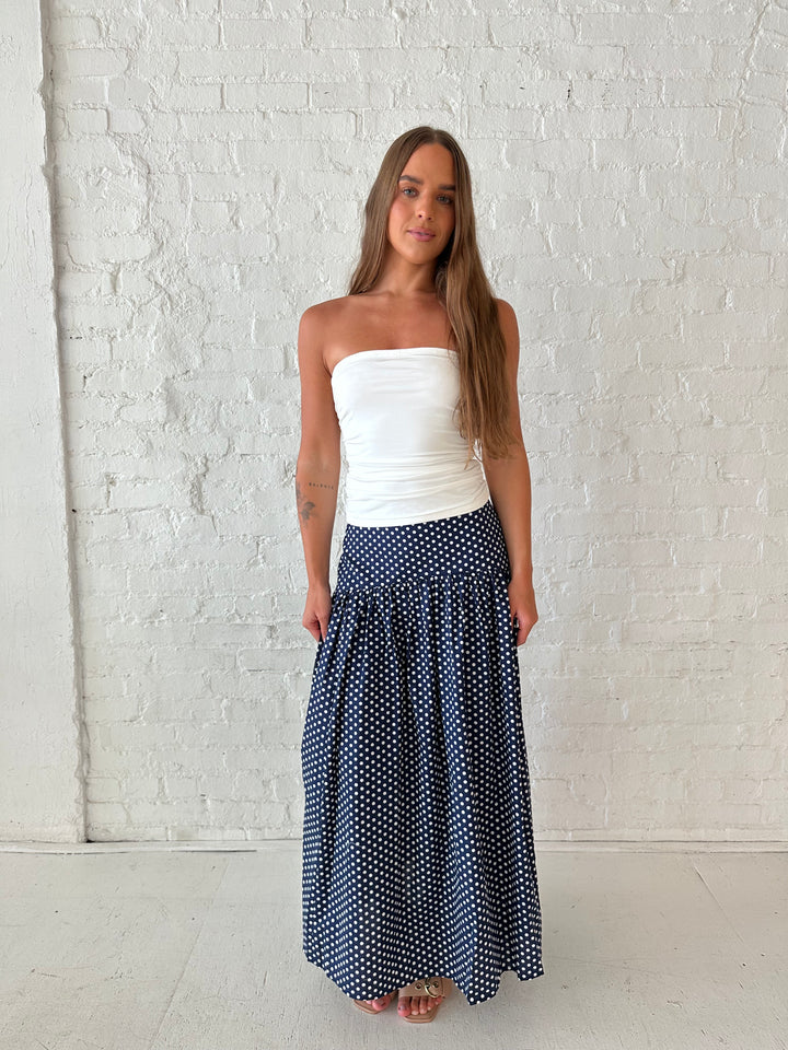 Woman wearing navy polka dot maxi skirt with white ruched tube top.