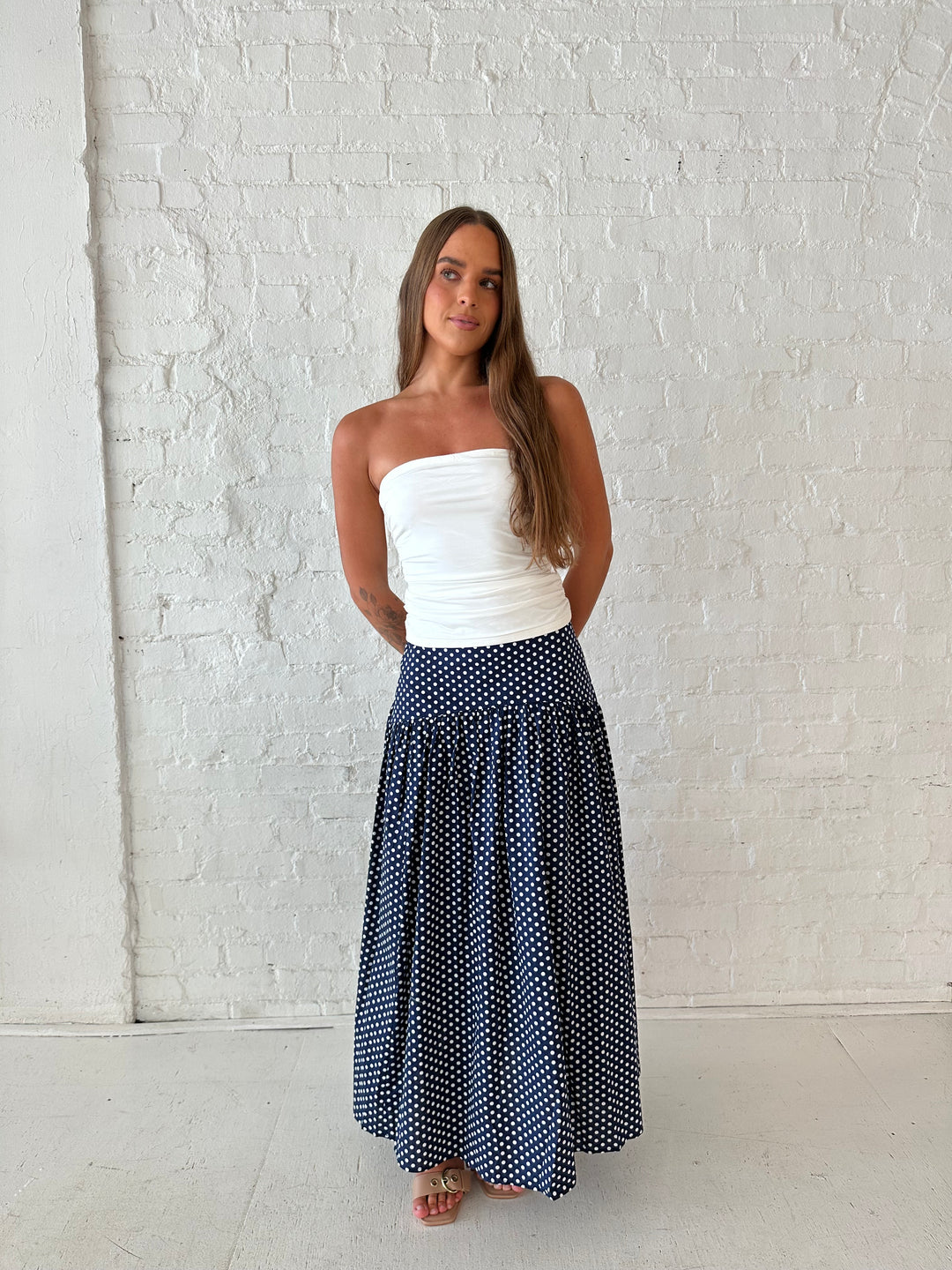 Woman wearing navy polka dot maxi skirt with white ruched tube top.