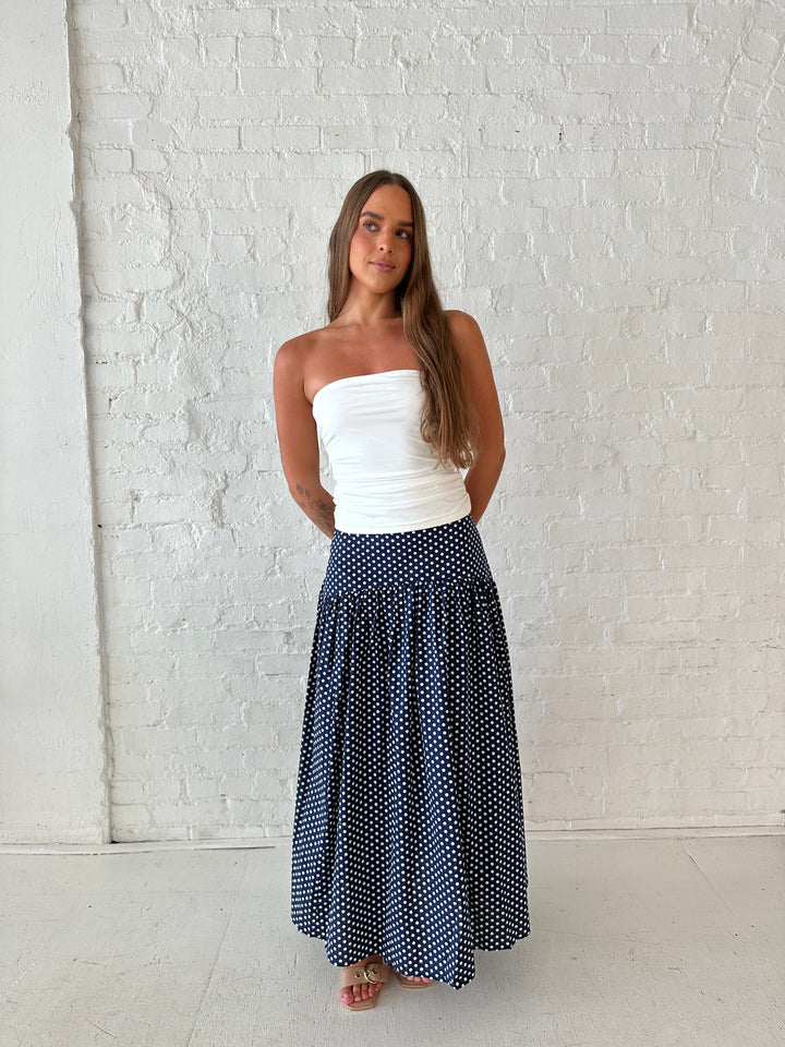 Woman wearing navy polka dot maxi skirt with white ruched tube top.