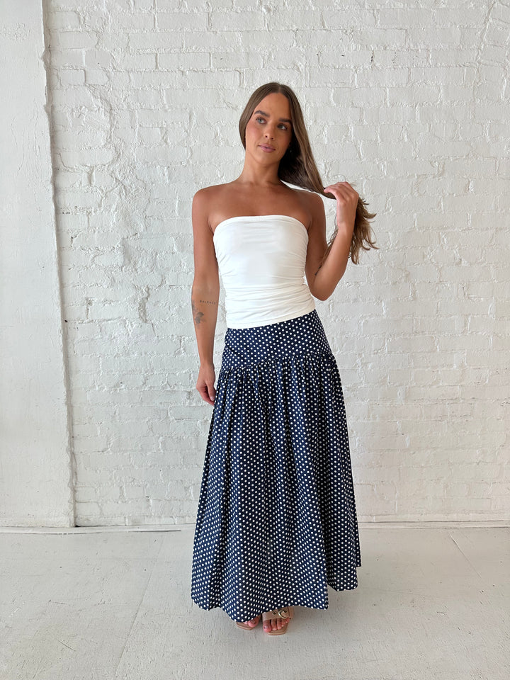 Woman wearing navy polka dot maxi skirt with white ruched tube top.