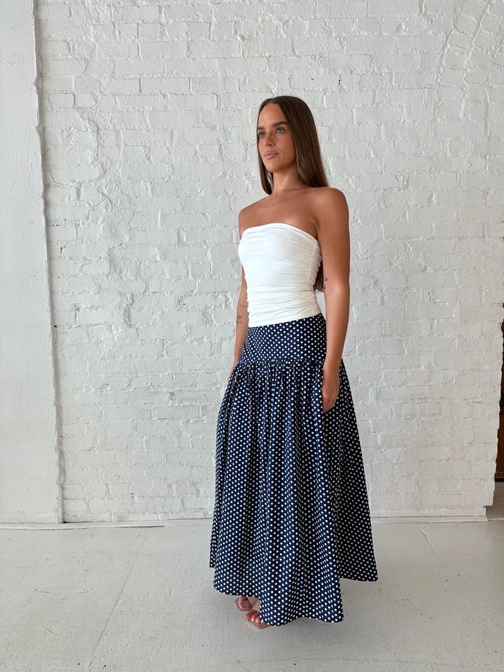 Woman wearing navy polka dot maxi skirt with white ruched tube top.