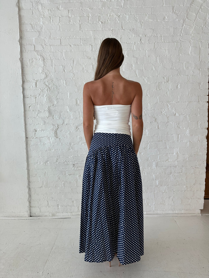 Woman wearing navy polka dot maxi skirt with white ruched tube top.