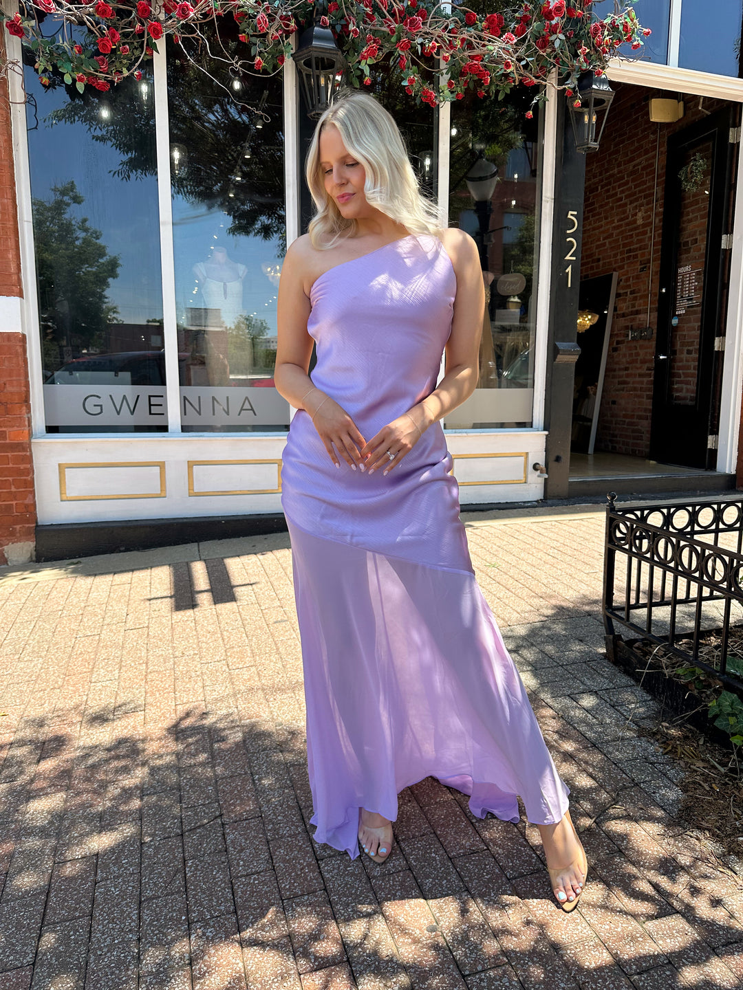 Woman wearing one shoulder lavender maxi dress with sheer leg paneling, open back, and strap detailing.