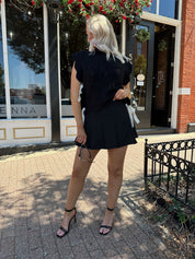 Woman wearing black cable knit sleeveless sweater with contrast bow back. 