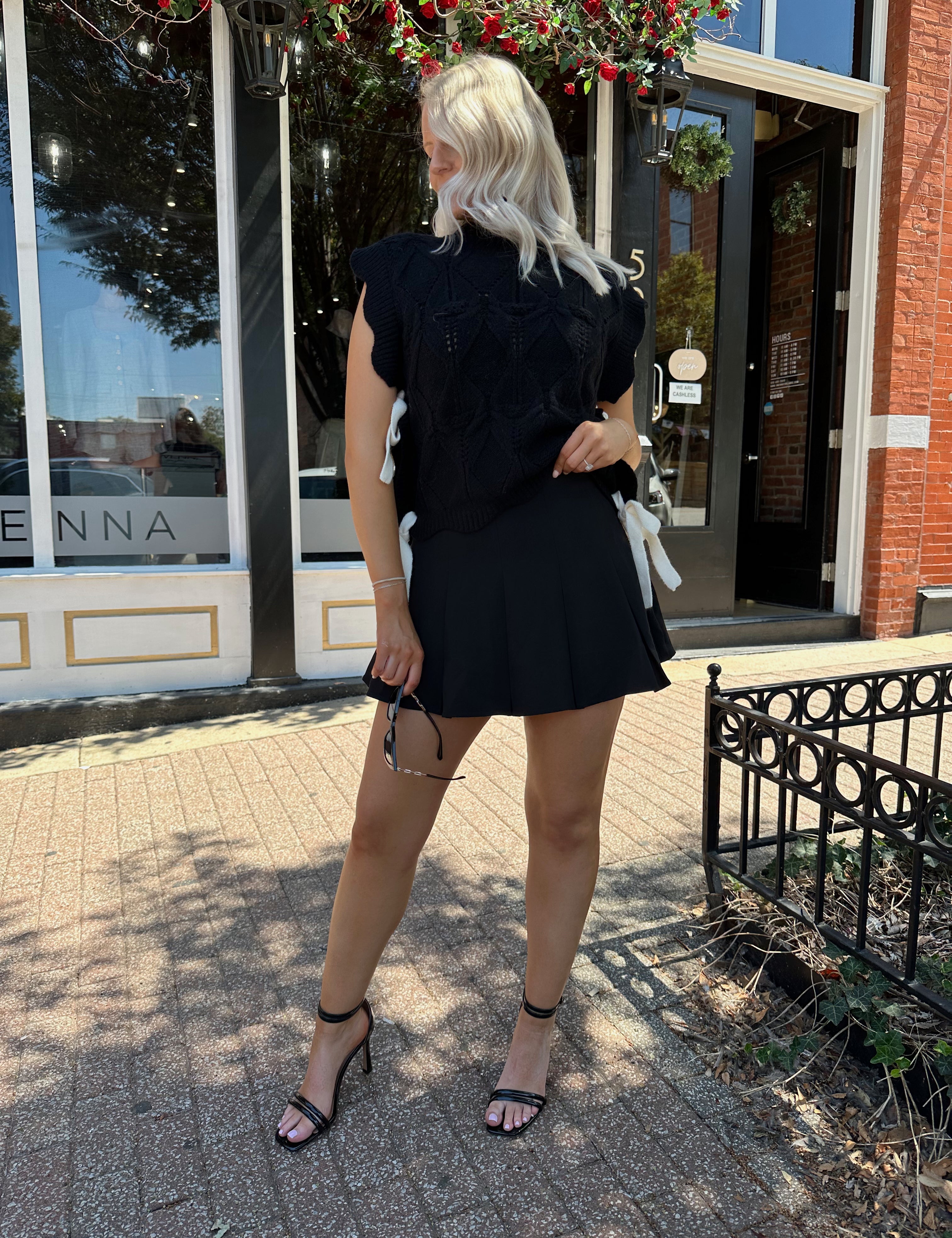 Woman wearing black cable knit sleeveless sweater with contrast bow back. 