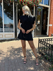Woman wearing black cable knit sleeveless sweater with contrast bow back. 