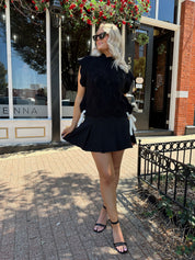 Woman wearing black cable knit sleeveless sweater with contrast bow back. 