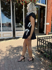 Woman wearing black cable knit sleeveless sweater with contrast bow back. 