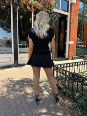 Woman wearing black cable knit sleeveless sweater with contrast bow back. 