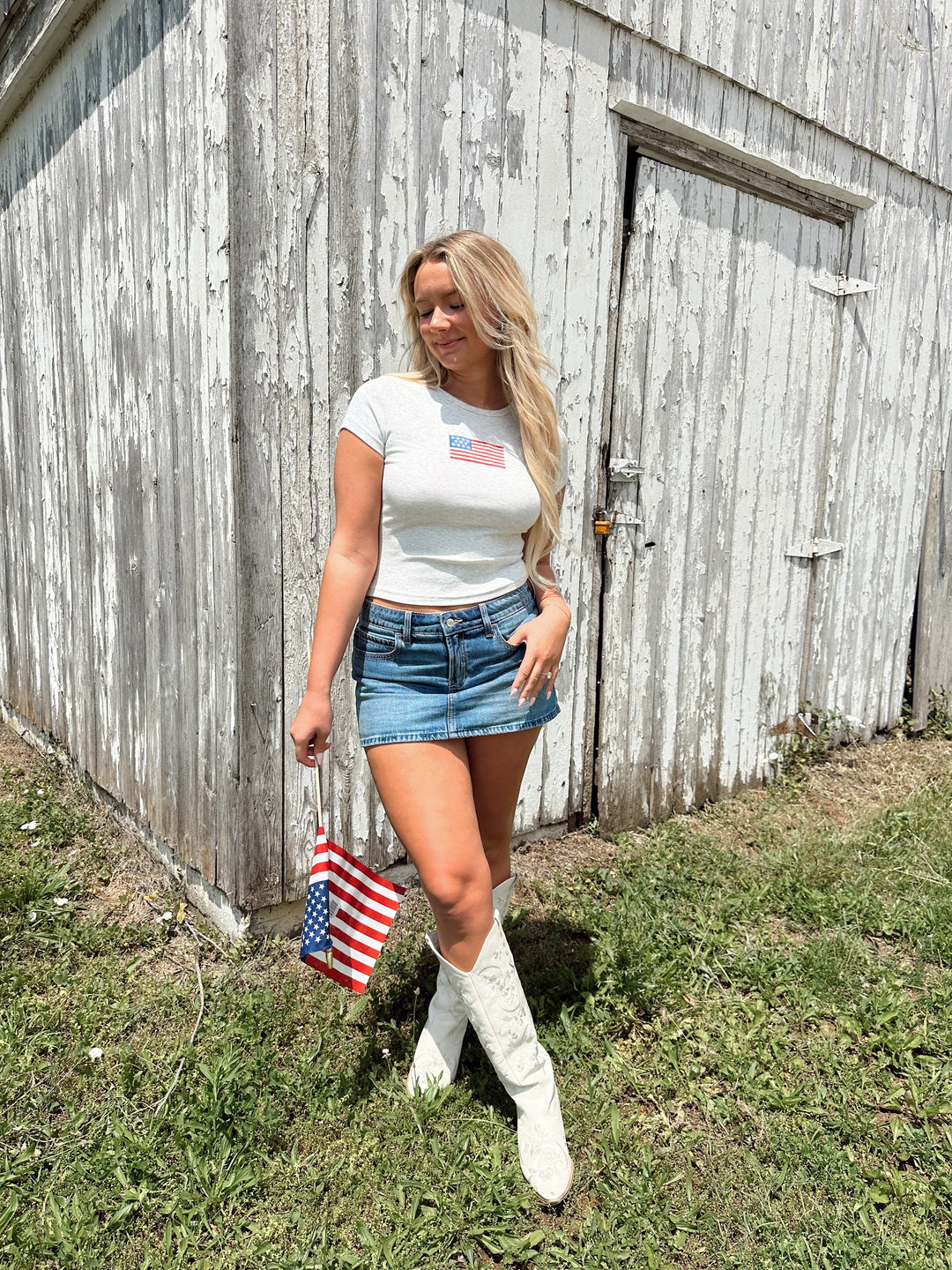 Woman wearing a light grey baby tee with an embroidered American flag on the chest