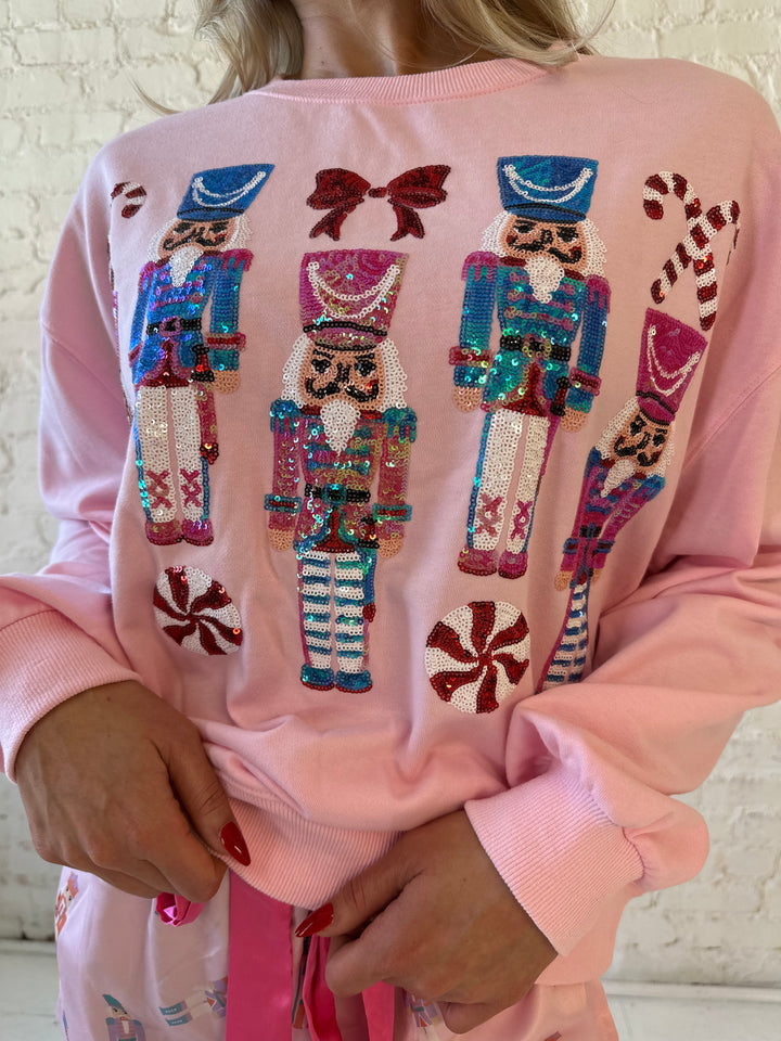 Woman wearing light pink oversized sweater with sequin nutcrackers on the front. 