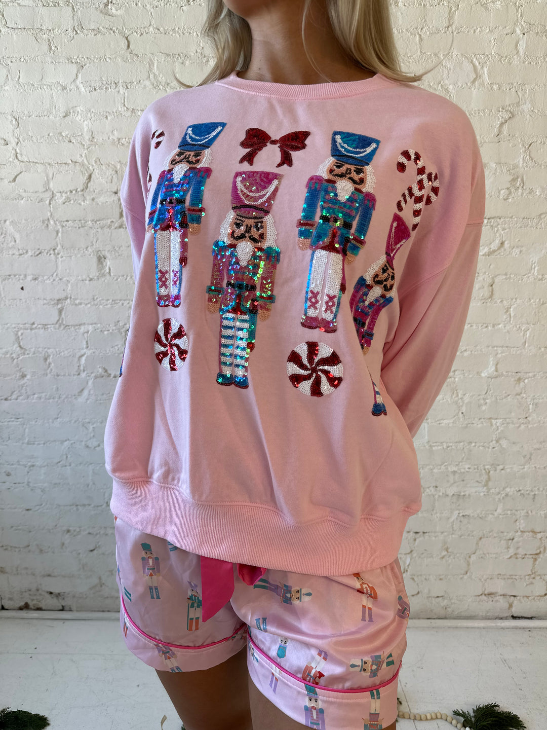 Woman wearing light pink oversized sweater with sequin nutcrackers on the front. 