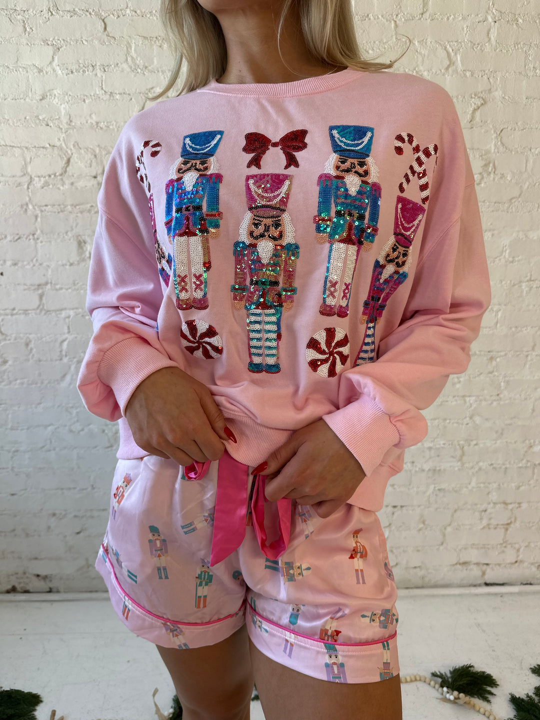 Woman wearing light pink oversized sweater with sequin nutcrackers on the front. 