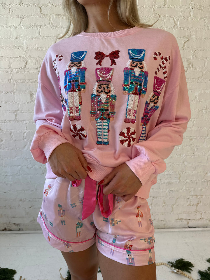 Woman wearing light pink oversized sweater with sequin nutcrackers on the front. 