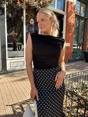 Woman wearing black ruched sleeveless top with polka dot maxi skirt. 