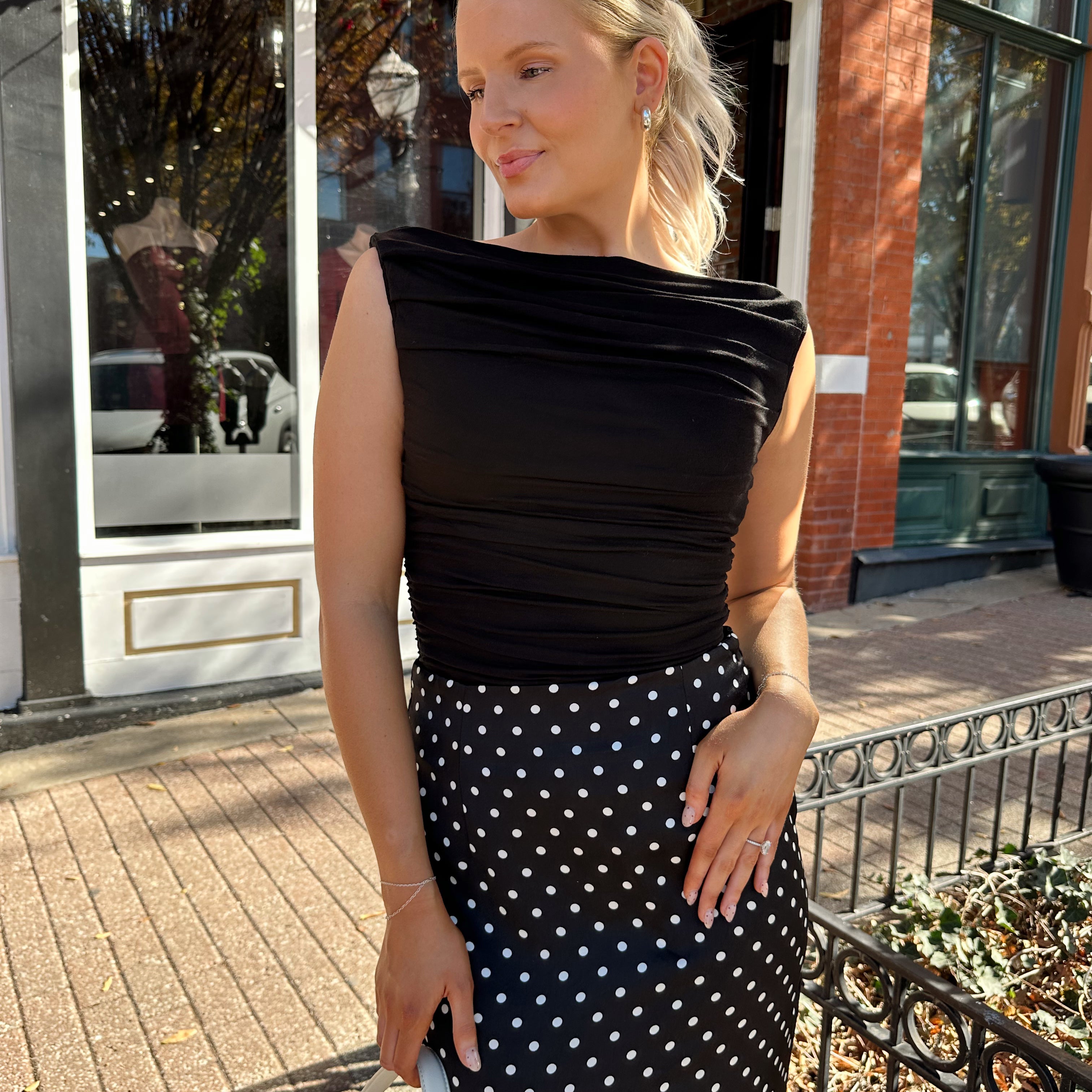 Woman wearing black ruched sleeveless top with polka dot maxi skirt. 