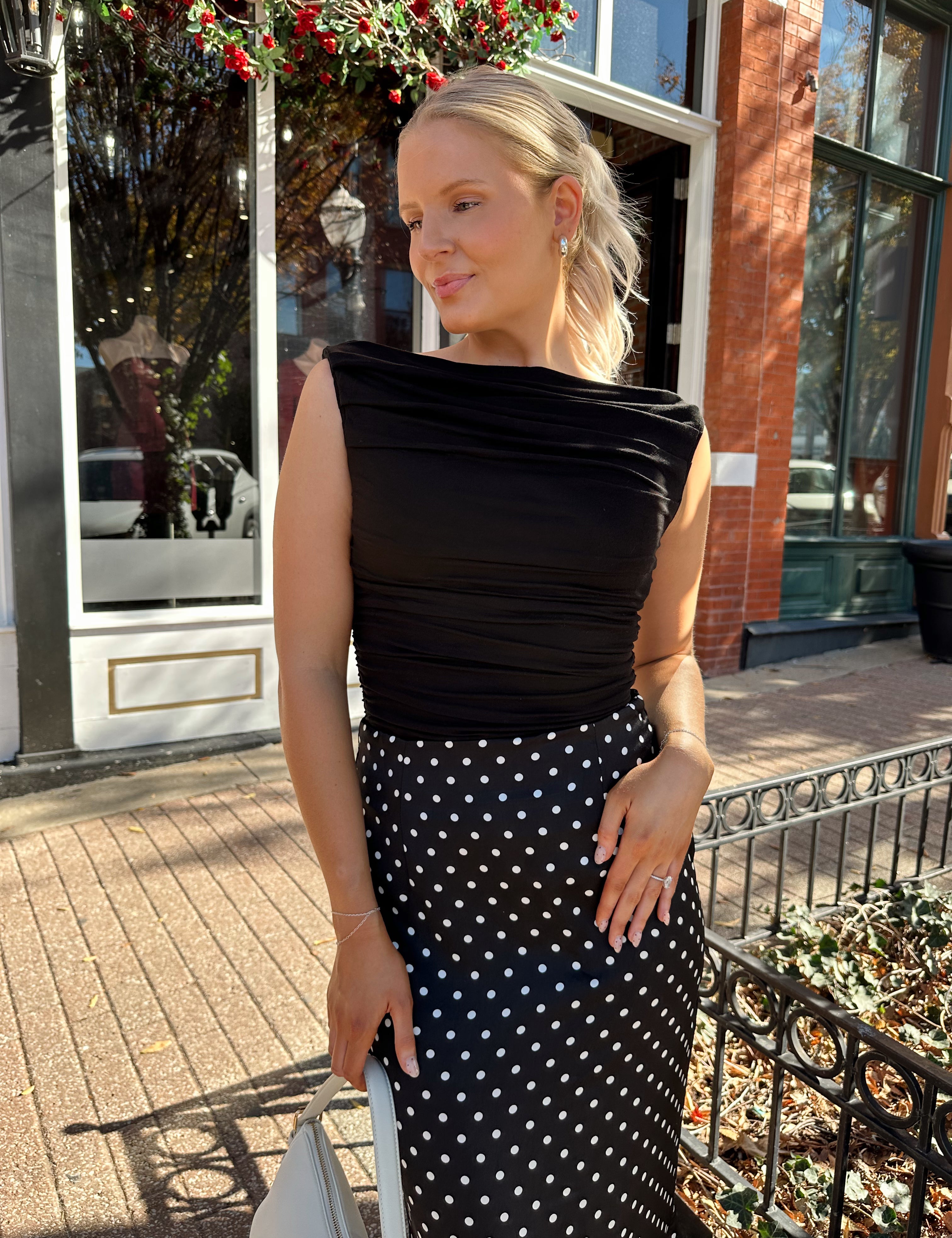 Woman wearing black ruched sleeveless top with polka dot maxi skirt. 