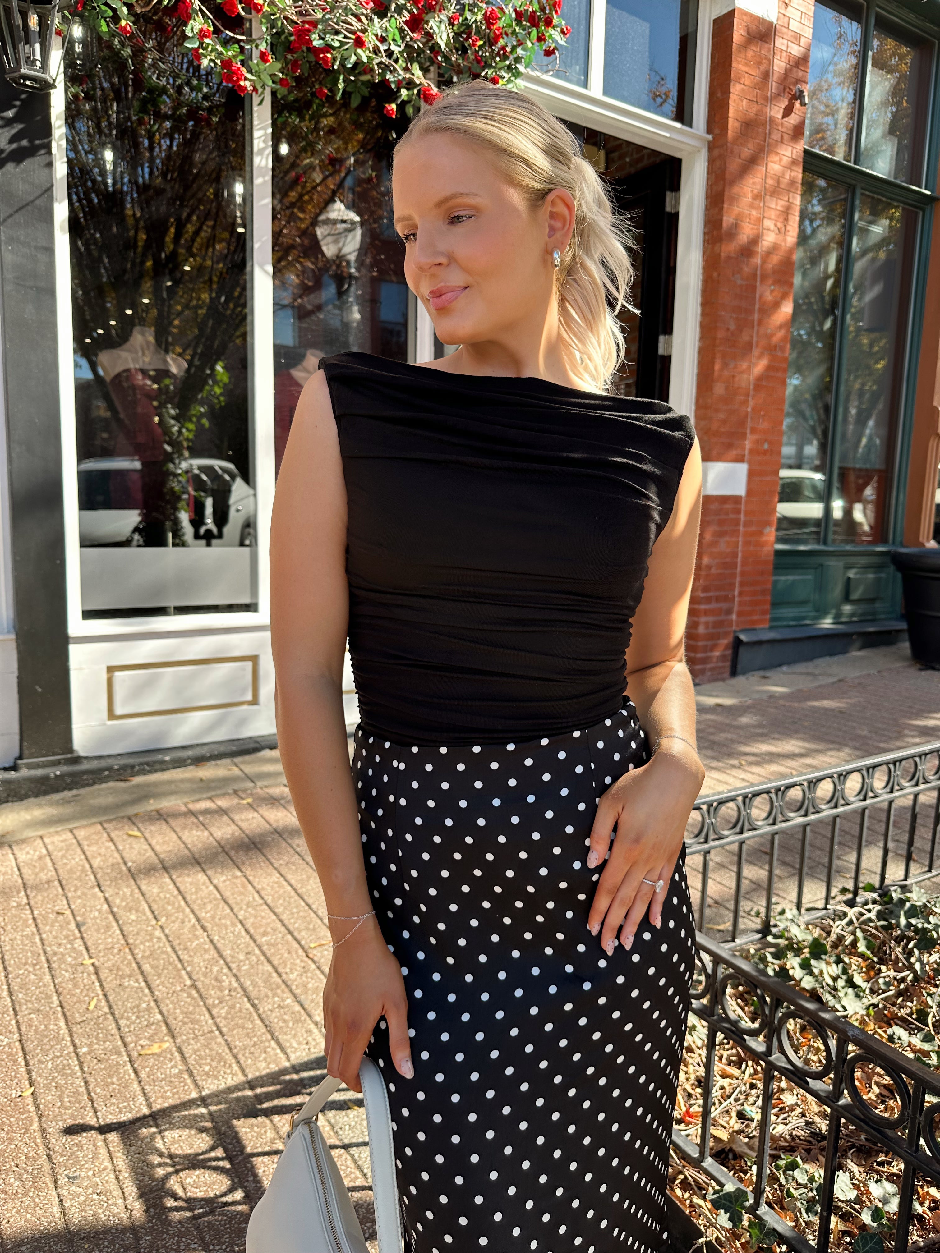 Woman wearing black ruched sleeveless top with polka dot maxi skirt. 