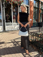 Woman wearing black ruched sleeveless top with polka dot maxi skirt. 