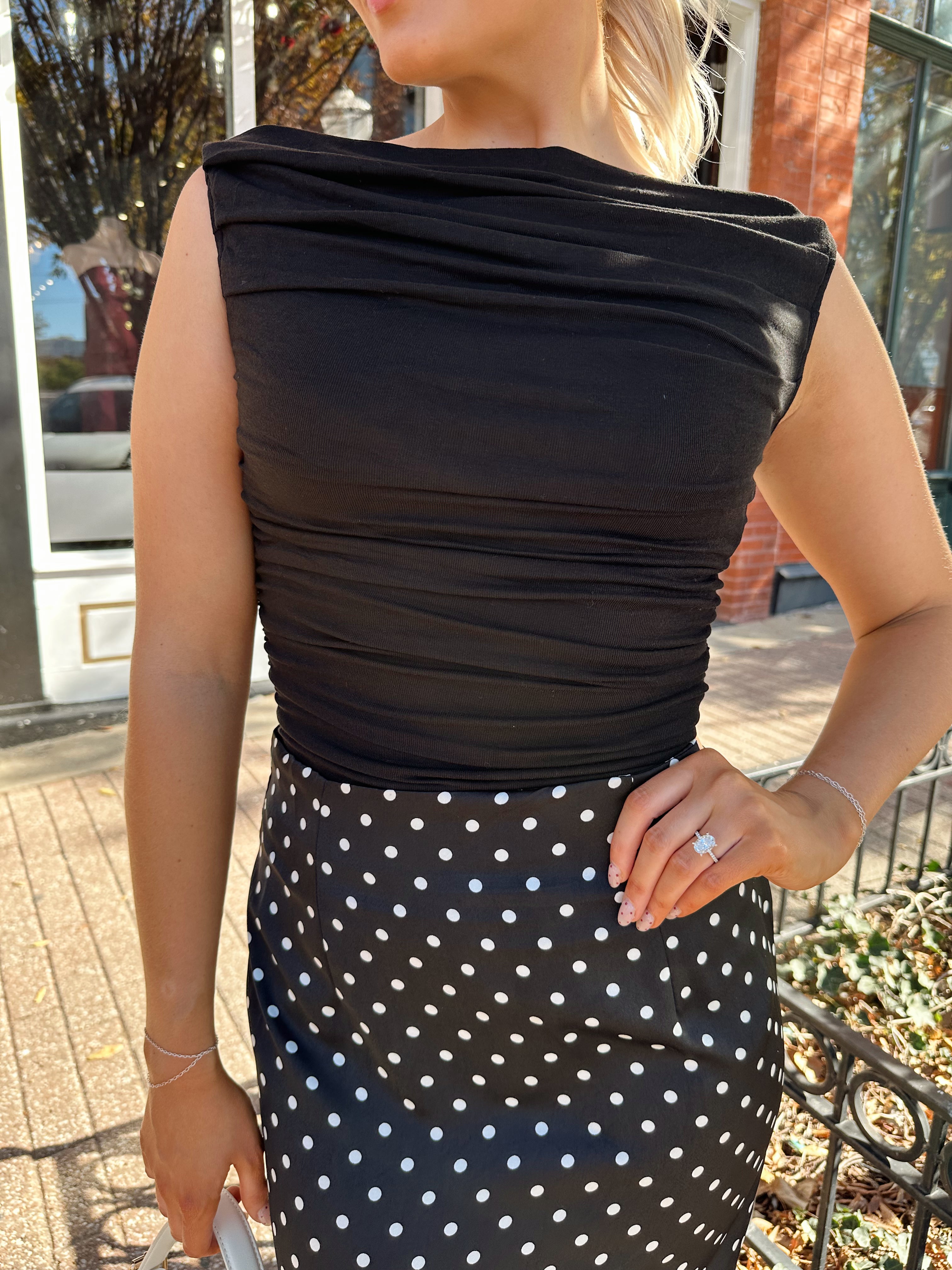 Woman wearing black ruched sleeveless top with polka dot maxi skirt. 