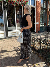 Woman wearing black ruched sleeveless top with polka dot maxi skirt. 