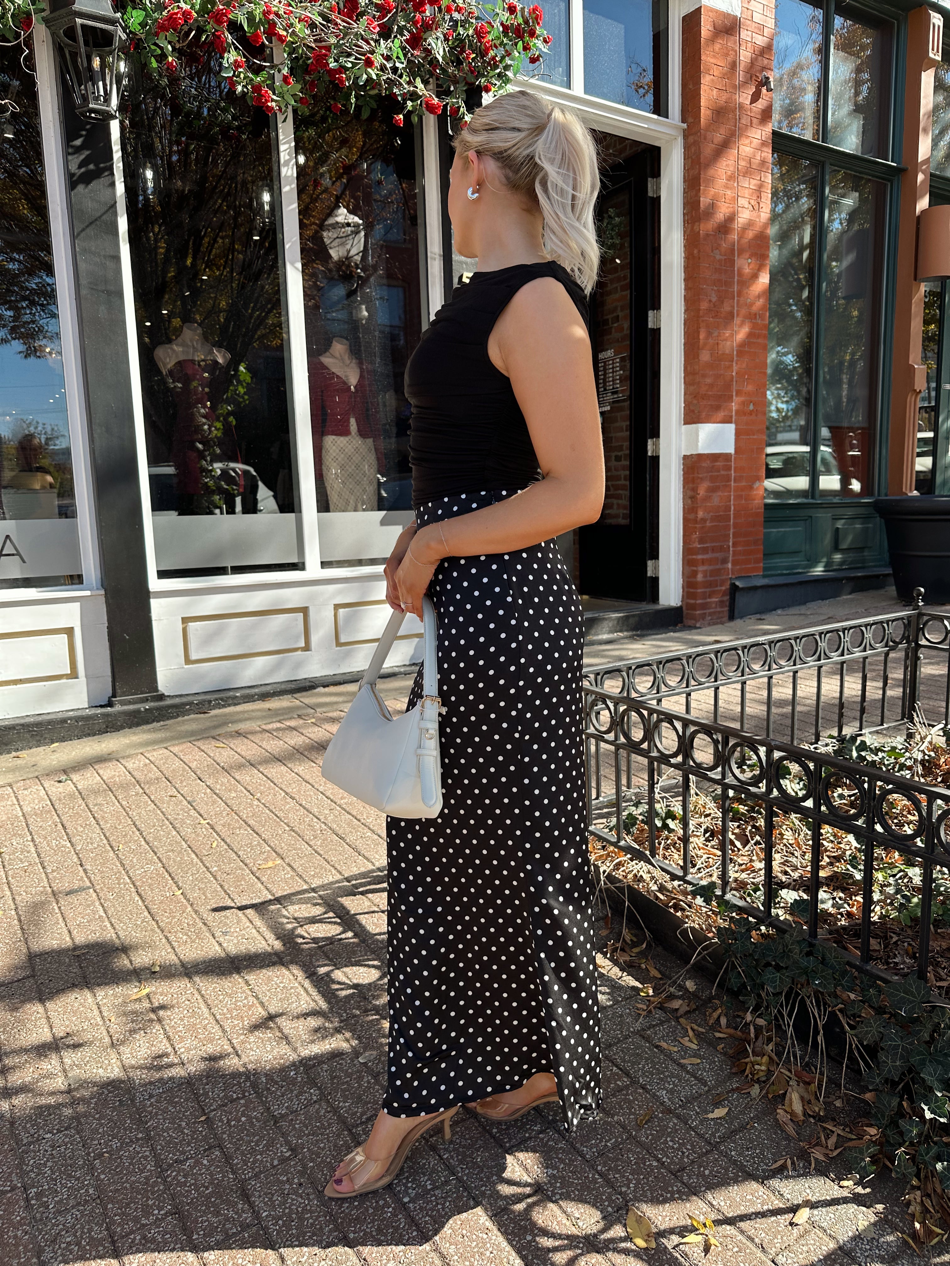 Woman wearing black ruched sleeveless top with polka dot maxi skirt. 