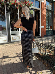 Woman wearing black ruched sleeveless top with polka dot maxi skirt. 