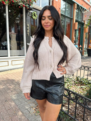 Woman wearing blush colored knit button down cardigan with black leather shorts.