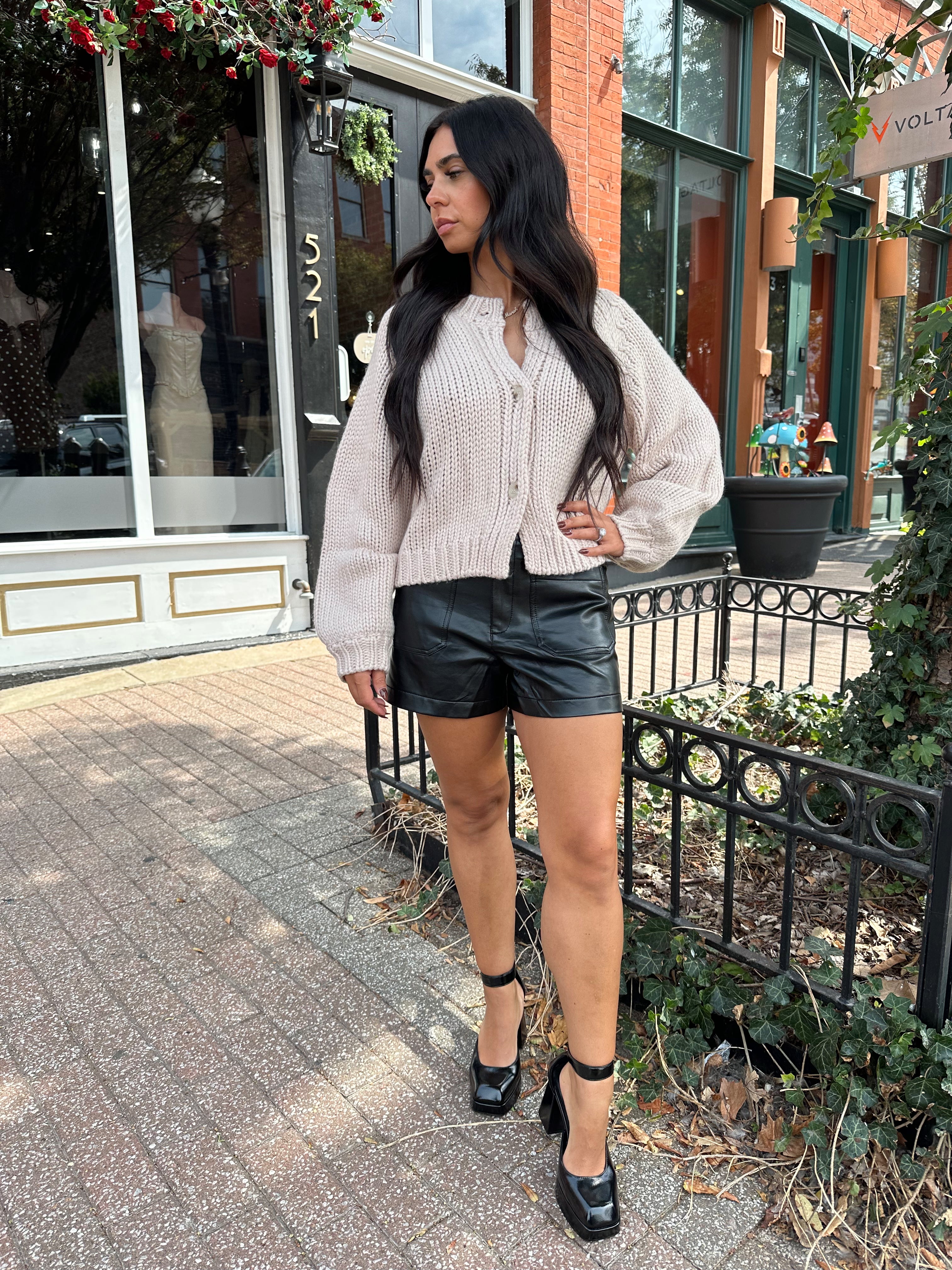 Woman wearing blush colored knit button down cardigan with black leather shorts.