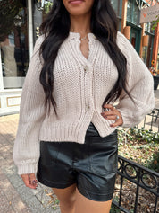 Woman wearing blush colored knit button down cardigan with black leather shorts.