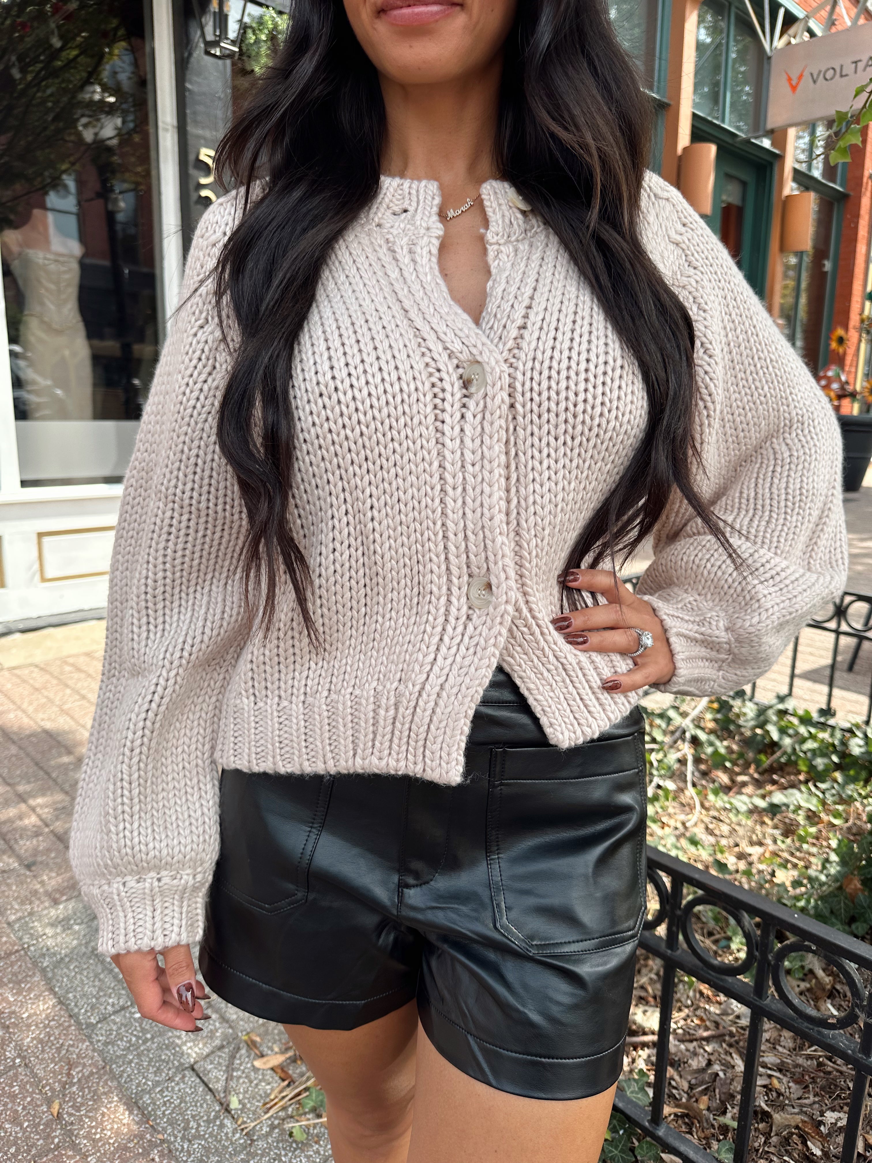 Woman wearing blush colored knit button down cardigan with black leather shorts.